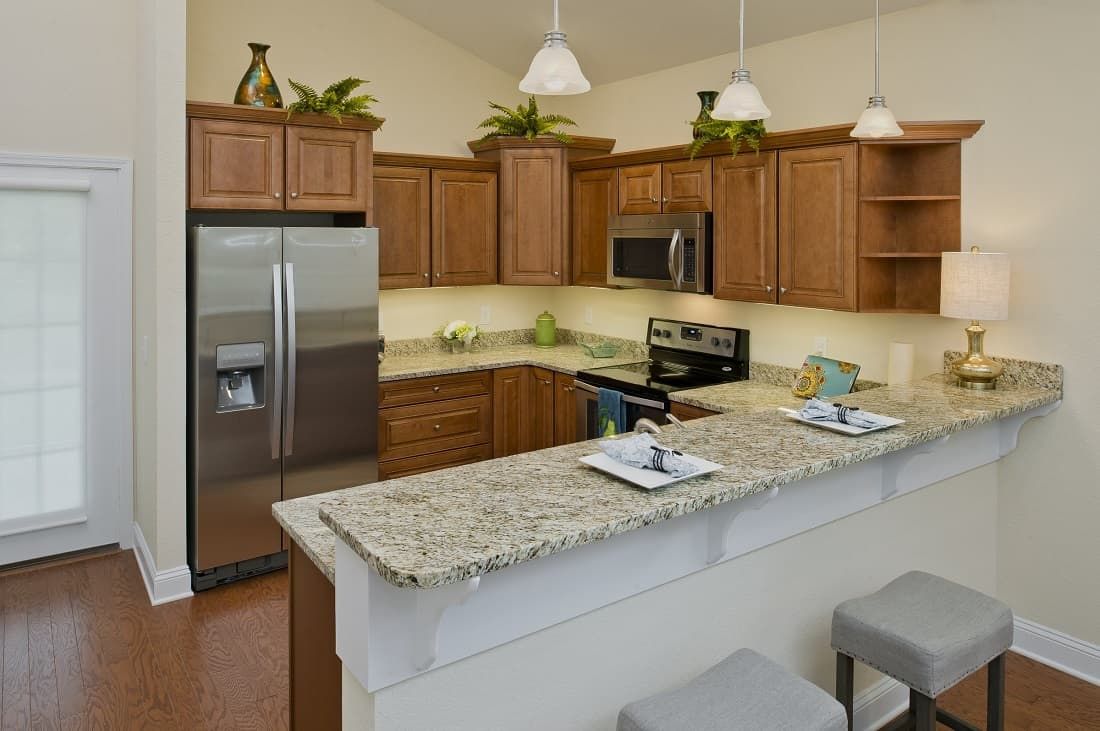 A modern kitchen with wooden cabinets and a granite countertop, featuring stainless steel appliances and pendant lighting.