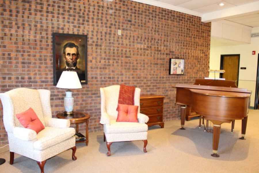 A cozy living room featuring a brick wall, two armchairs, a grand piano, and decorative artwork.