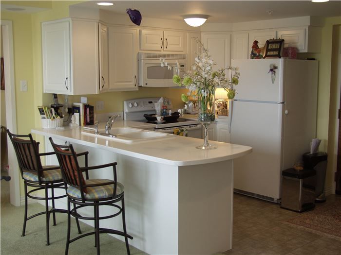 A modern kitchen featuring white cabinets, a large countertop with bar stools, and decorative flowers.