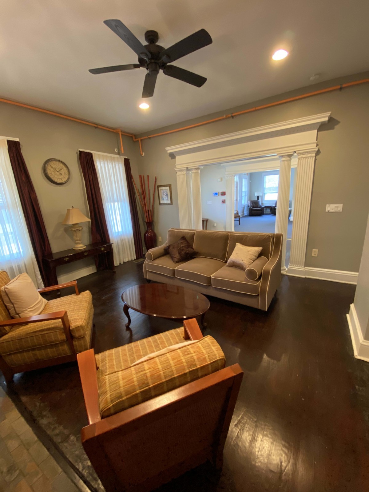 A cozy living room with a sofa, two armchairs, and a coffee table, featuring hardwood floors and a ceiling fan.