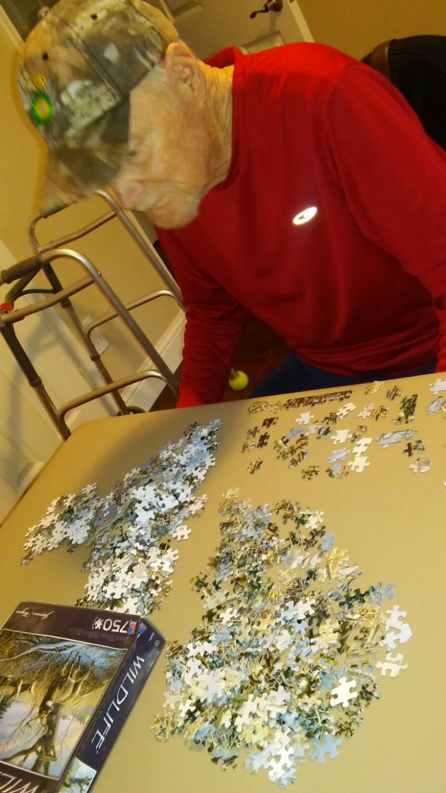 An elderly person working on a jigsaw puzzle at a table indoors.