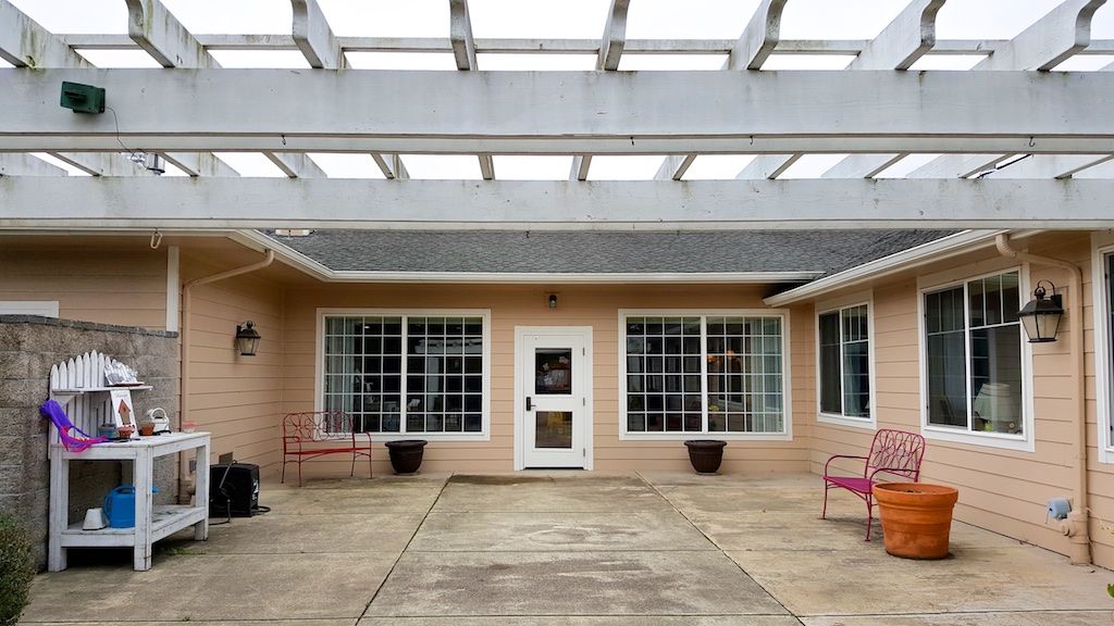 A courtyard with large windows, a central door, and benches on either side.