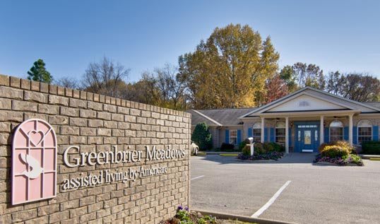 A brick sign in front of a building with a parking lot and trees in the background.