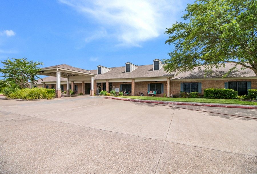 A wide-angle view of a building with a large driveway and surrounding greenery under a clear blue sky.