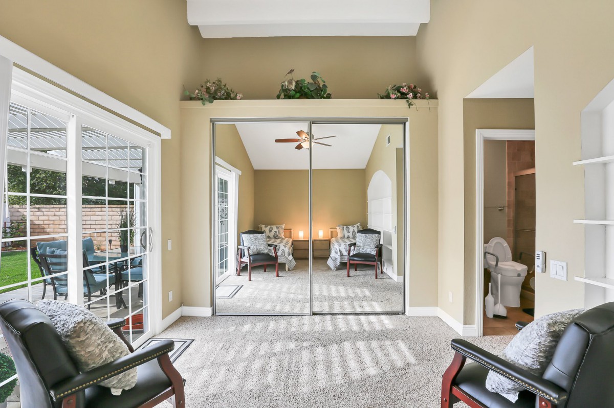 A cozy bedroom featuring a mirrored closet, beige walls, and comfortable seating with natural light streaming in.
