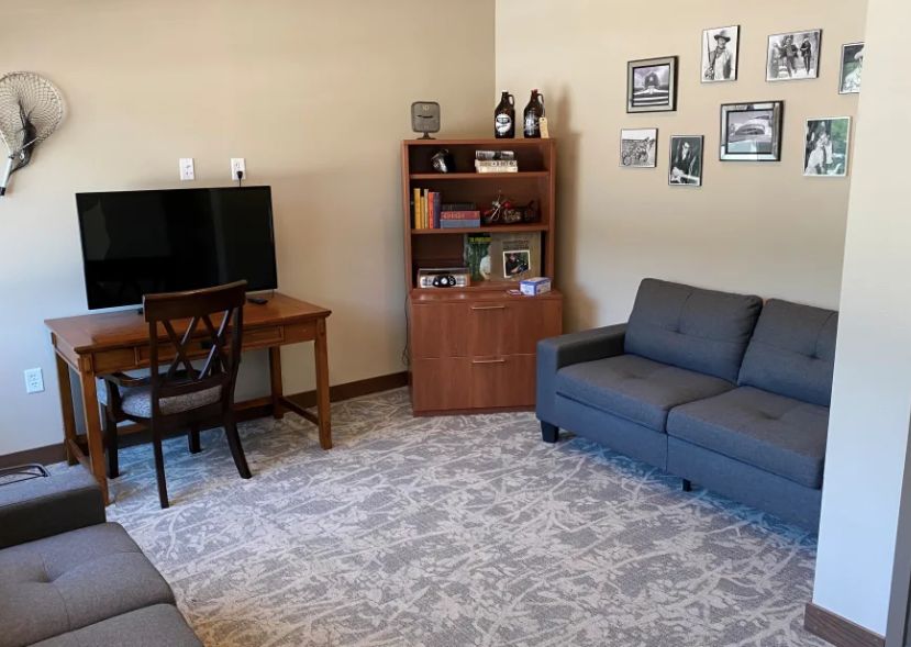 A cozy living room with a sofa, desk, bookshelf, and a television.