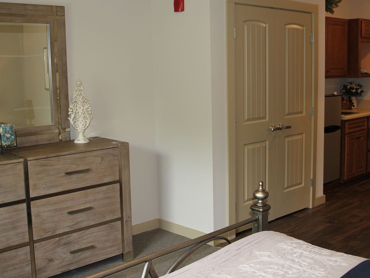 A cozy bedroom featuring a bed, a wooden dresser with a mirror, and closed doors.
