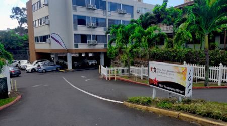 Entrance of a hospital building with palm trees and signage.