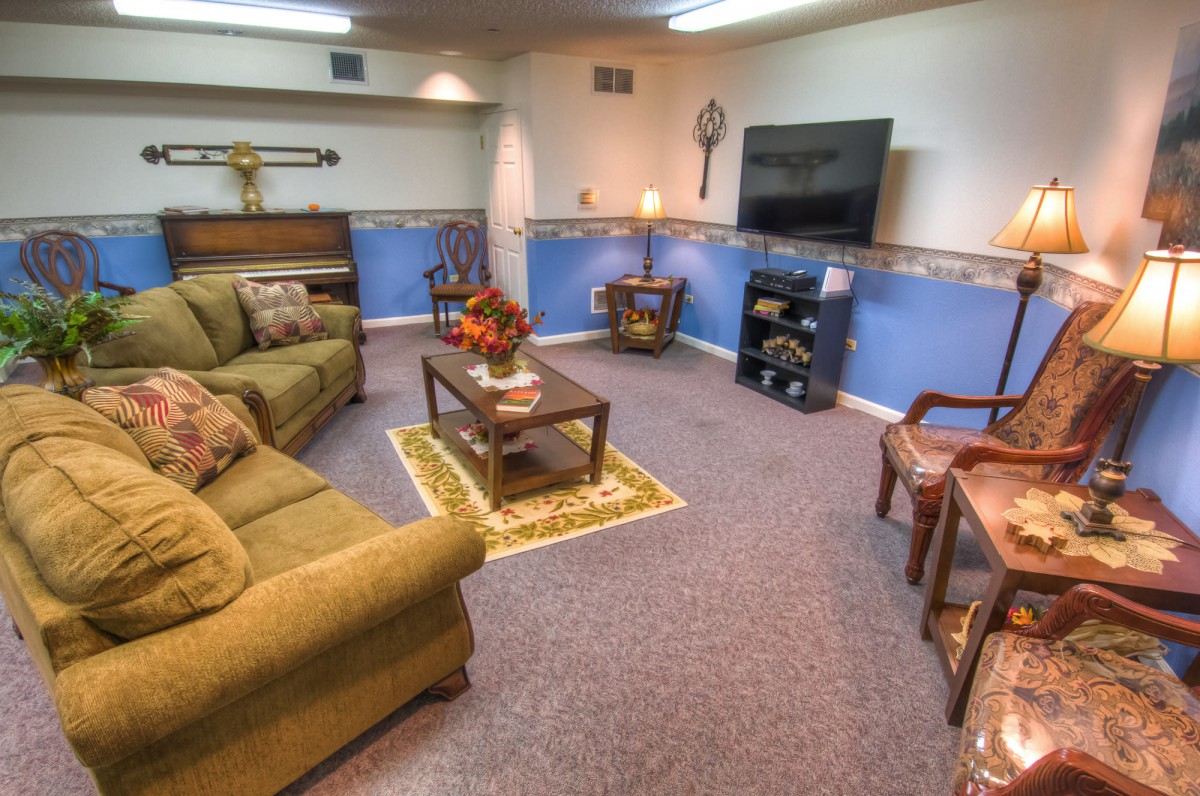 A cozy living room with a large green sofa, a TV mounted on the wall, and a coffee table in the center.