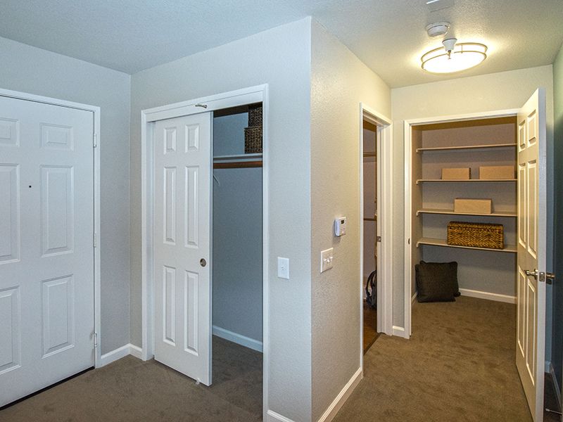 A room interior featuring a closet with sliding doors and an adjacent hallway leading to storage shelves, highlighted in neutral tones.
