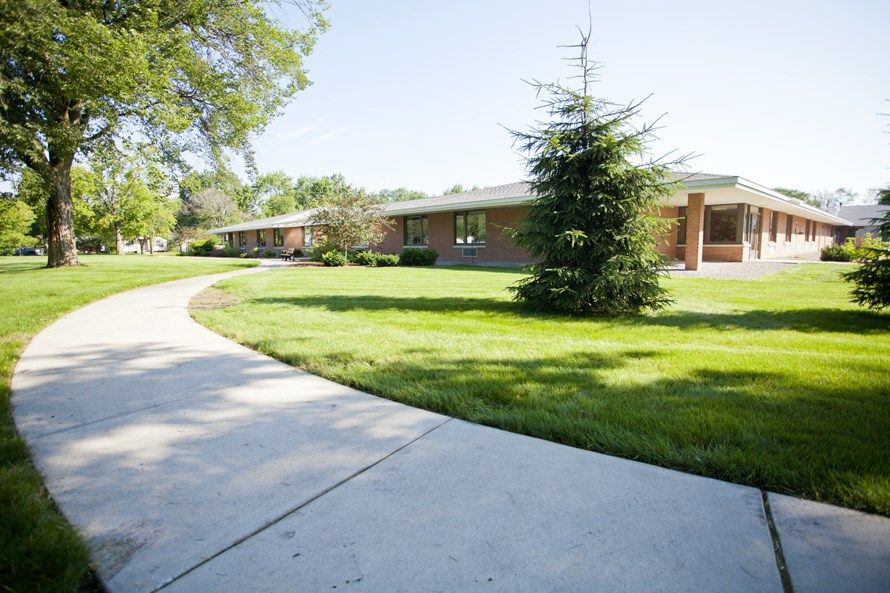 A scenic view of a building surrounded by lush green lawns and trees, with a curving sidewalk in the foreground.