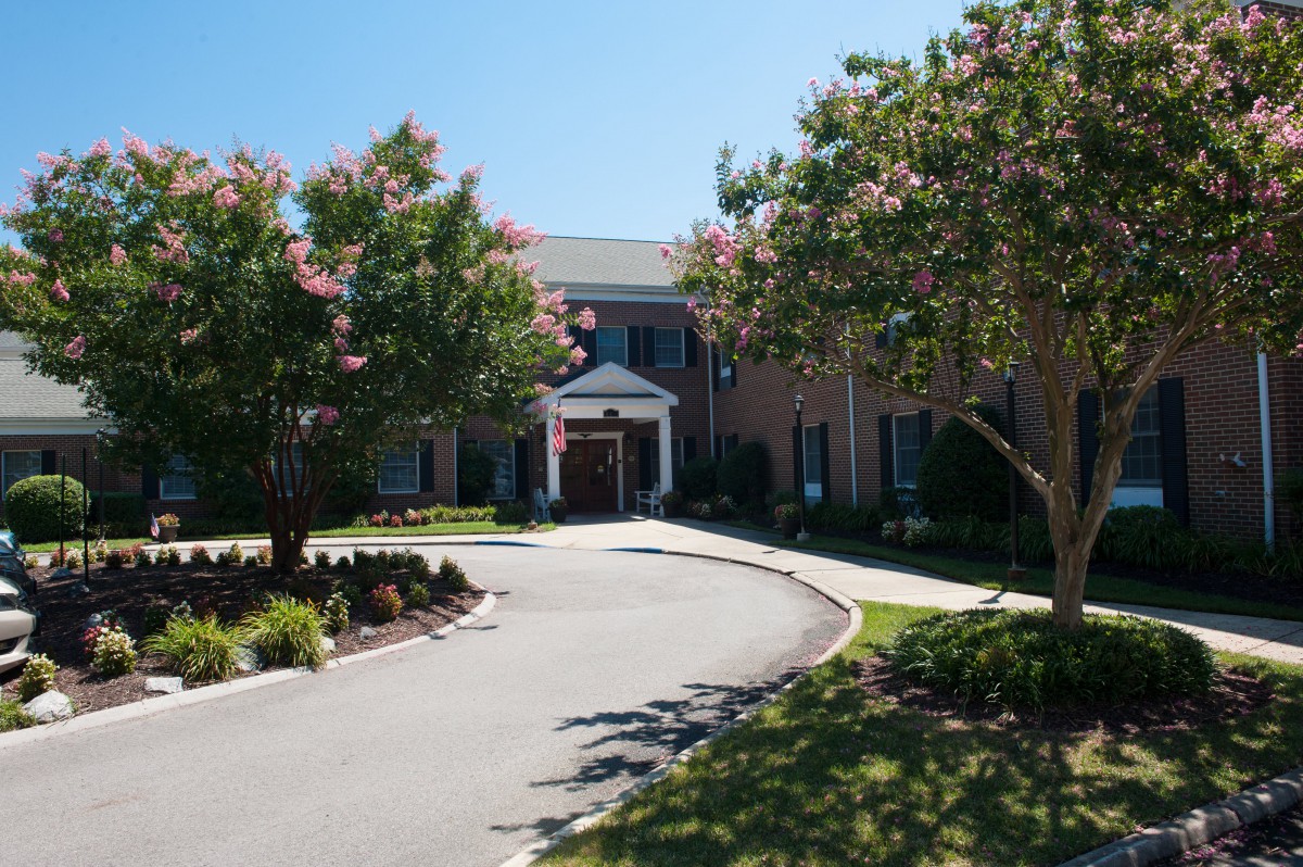 A large brick building with a circular driveway surrounded by well-maintained landscaping and trees on a sunny day.