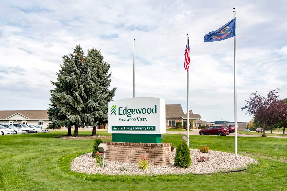 Outdoor sign for Edgewood, accompanied by flags nearby.