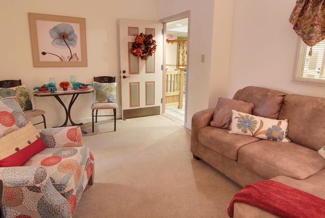 A cozy living room with colorful decor and a comfortable sofa, featuring an autumn-themed wreath on the door.