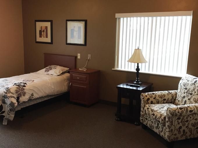 A cozy bedroom with a bed, bedside table, lamp, and armchair next to a window.