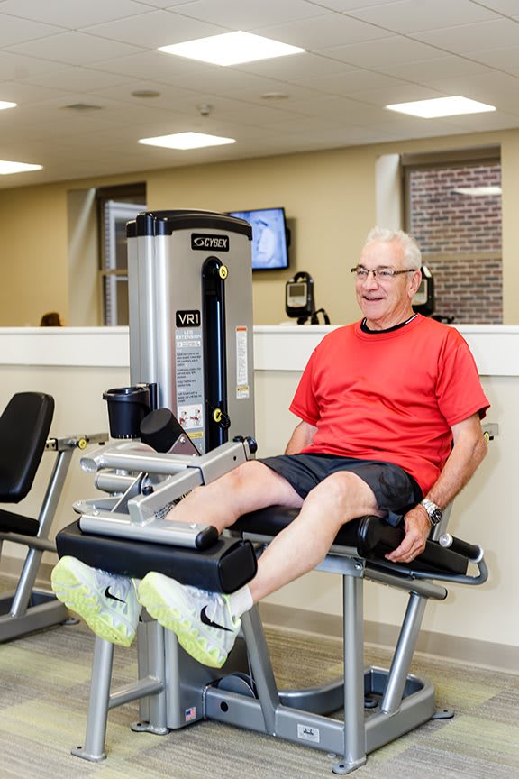 An elderly man exercises using a leg press machine in the gym, promoting an active lifestyle.