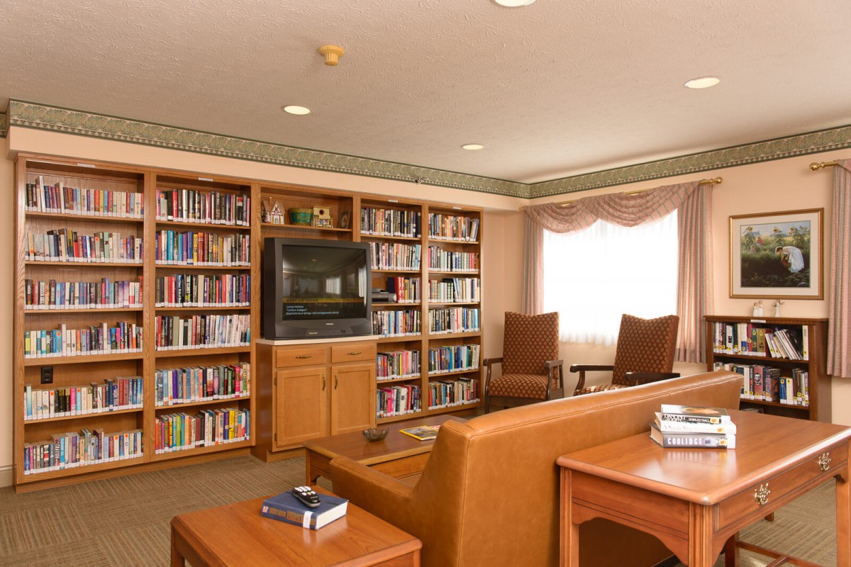 A cozy reading room with bookshelves, chairs, and a television.