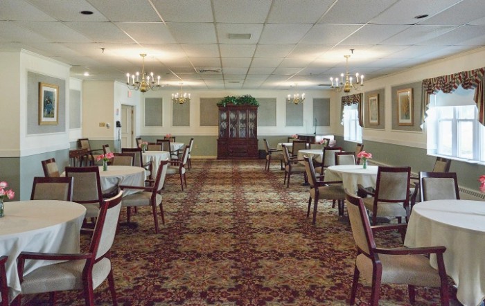 A spacious dining room with neatly arranged tables and chairs, illuminated by chandeliers.
