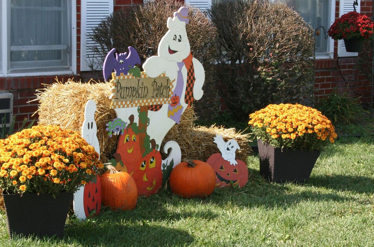 Festive Halloween display with ghosts, pumpkins, and hay bales surrounded by autumn flowers.