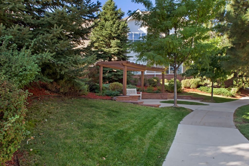 A serene garden area with a bench under a pergola surrounded by trees and landscaping.