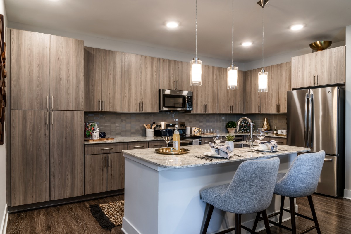 A modern kitchen with an island counter and wooden cabinets, featuring pendant lights and bar stools.