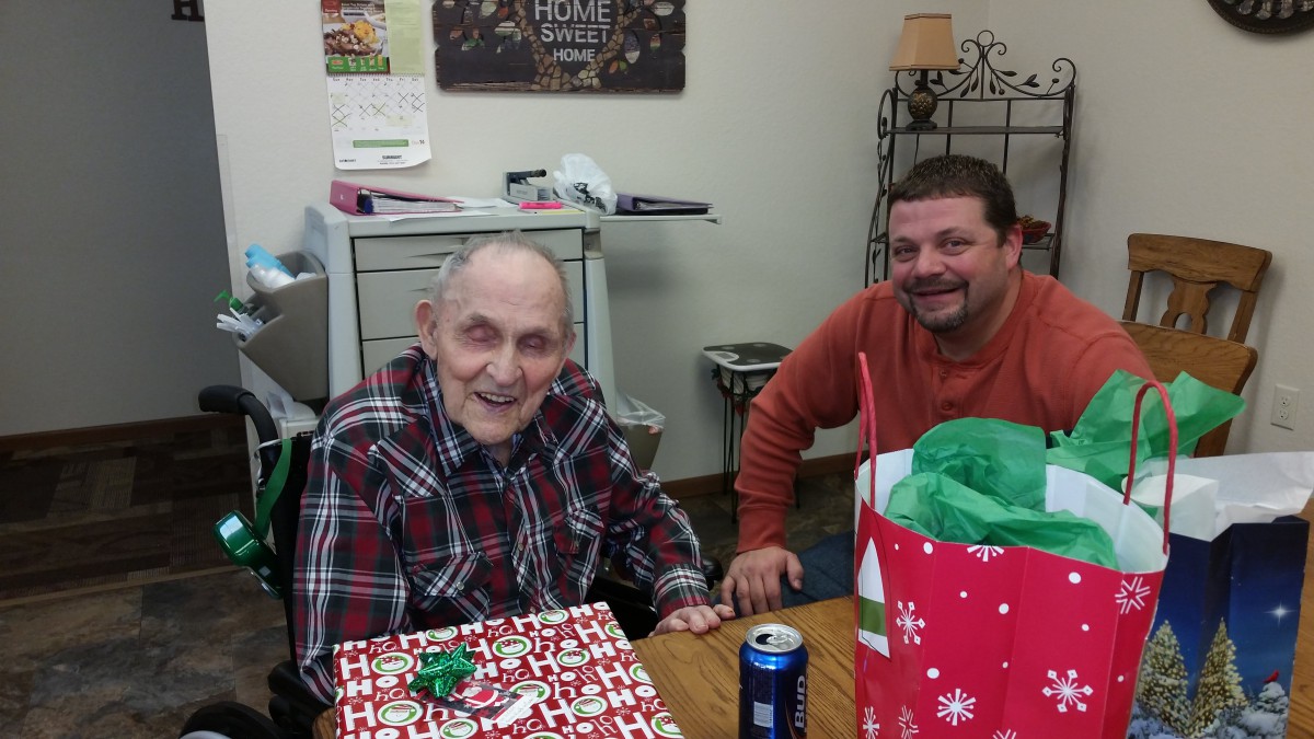 An elderly man and a younger man smiling at a table with gifts during a celebration.