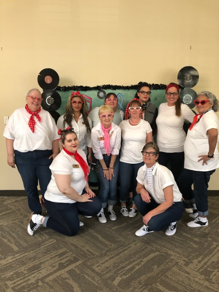 A group of people dressed in 1950s-themed costumes pose together for a photo at a retro-themed event.