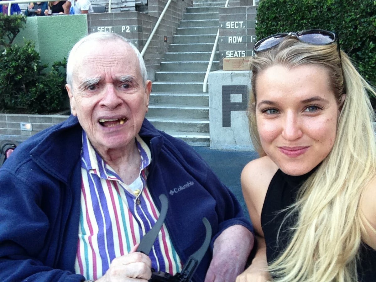 An elderly man and a woman take a selfie together outdoors.