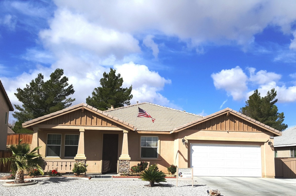 A suburban house with a garage, set against a bright blue sky with scattered clouds.