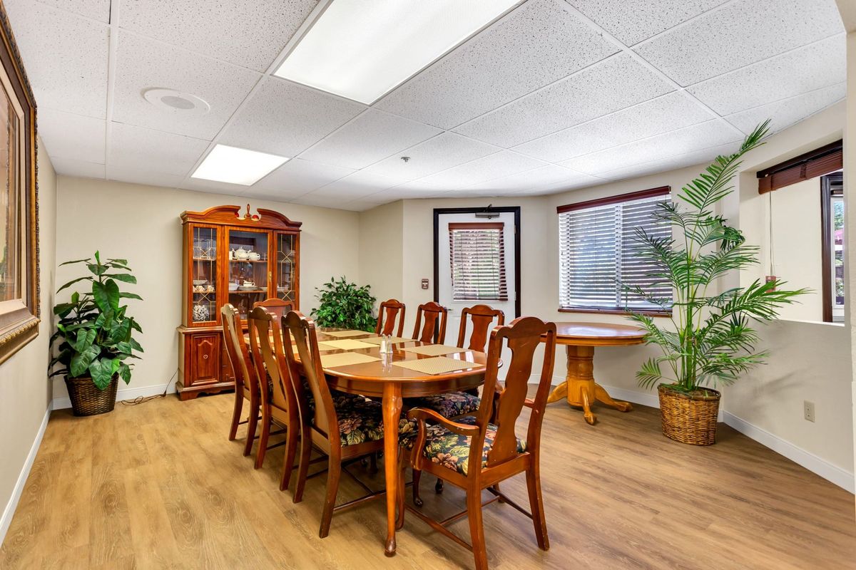 A spacious dining room with a wooden table and chairs, surrounded by indoor plants and natural lighting.