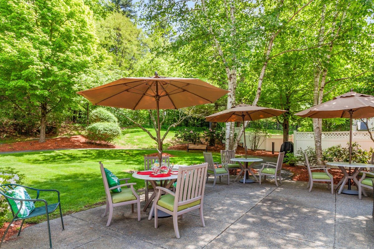 A sunny garden patio with tables, chairs, and umbrellas surrounded by lush greenery.
