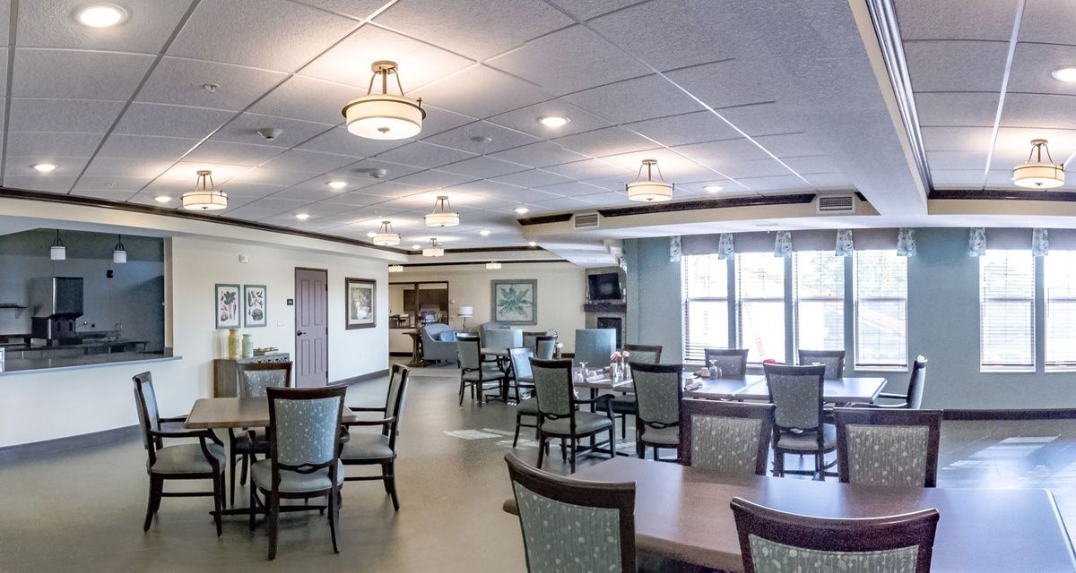 A spacious dining room with neatly arranged tables and chairs, featuring elegant lighting fixtures and large windows providing natural light.