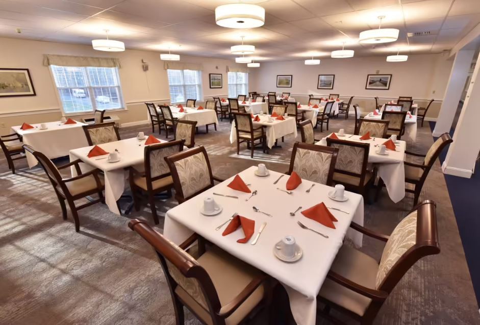 A well-lit dining room with tables neatly set, featuring folded napkins and comfortable chairs.