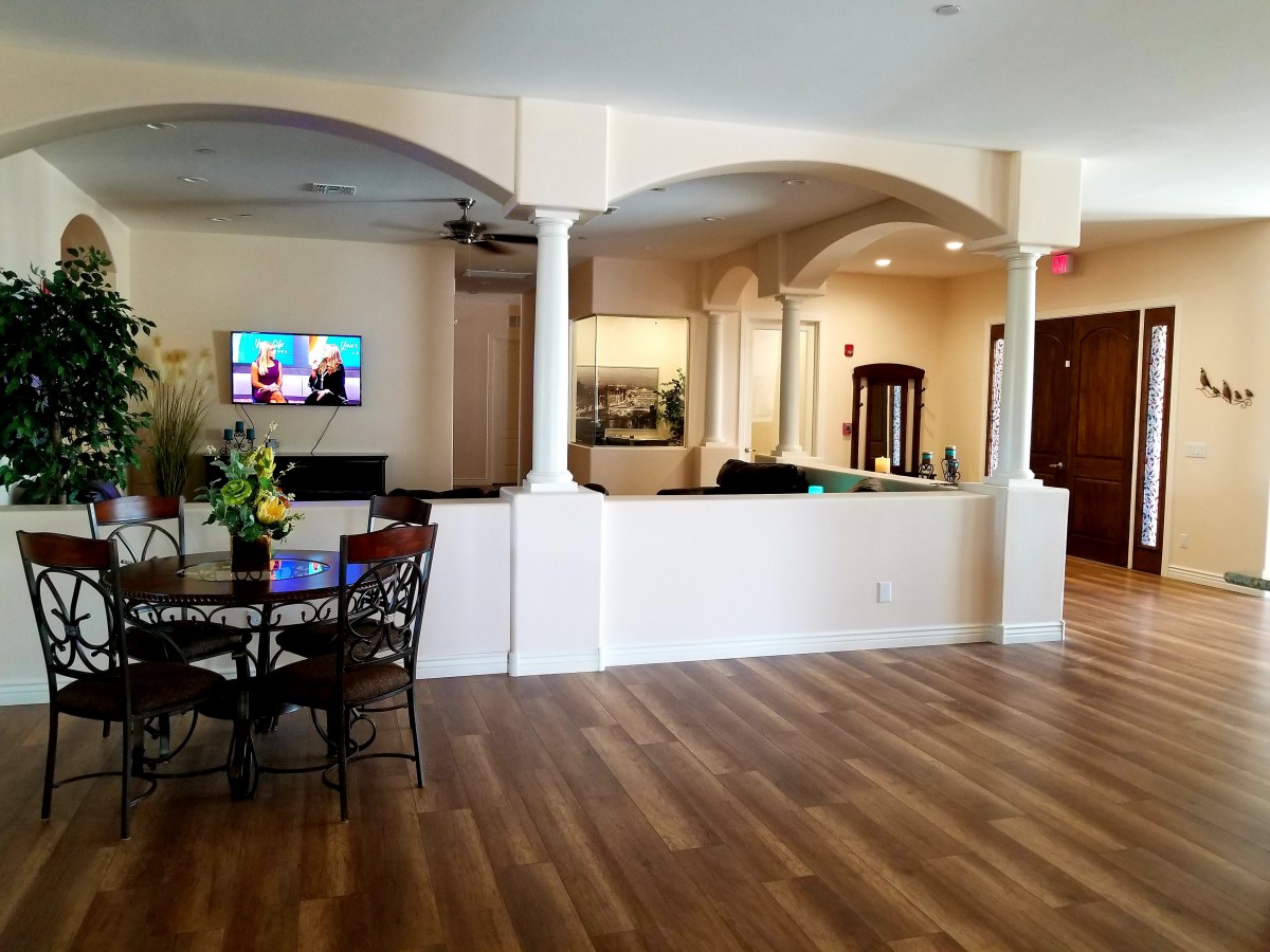 A spacious interior with a wooden floor, furnished with a table and chairs, featuring a wall-mounted television and decorative columns.
