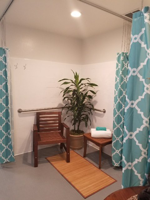 A bathroom shower area with teal patterned curtains, featuring a wooden bench, potted plant, and neatly folded towels.
