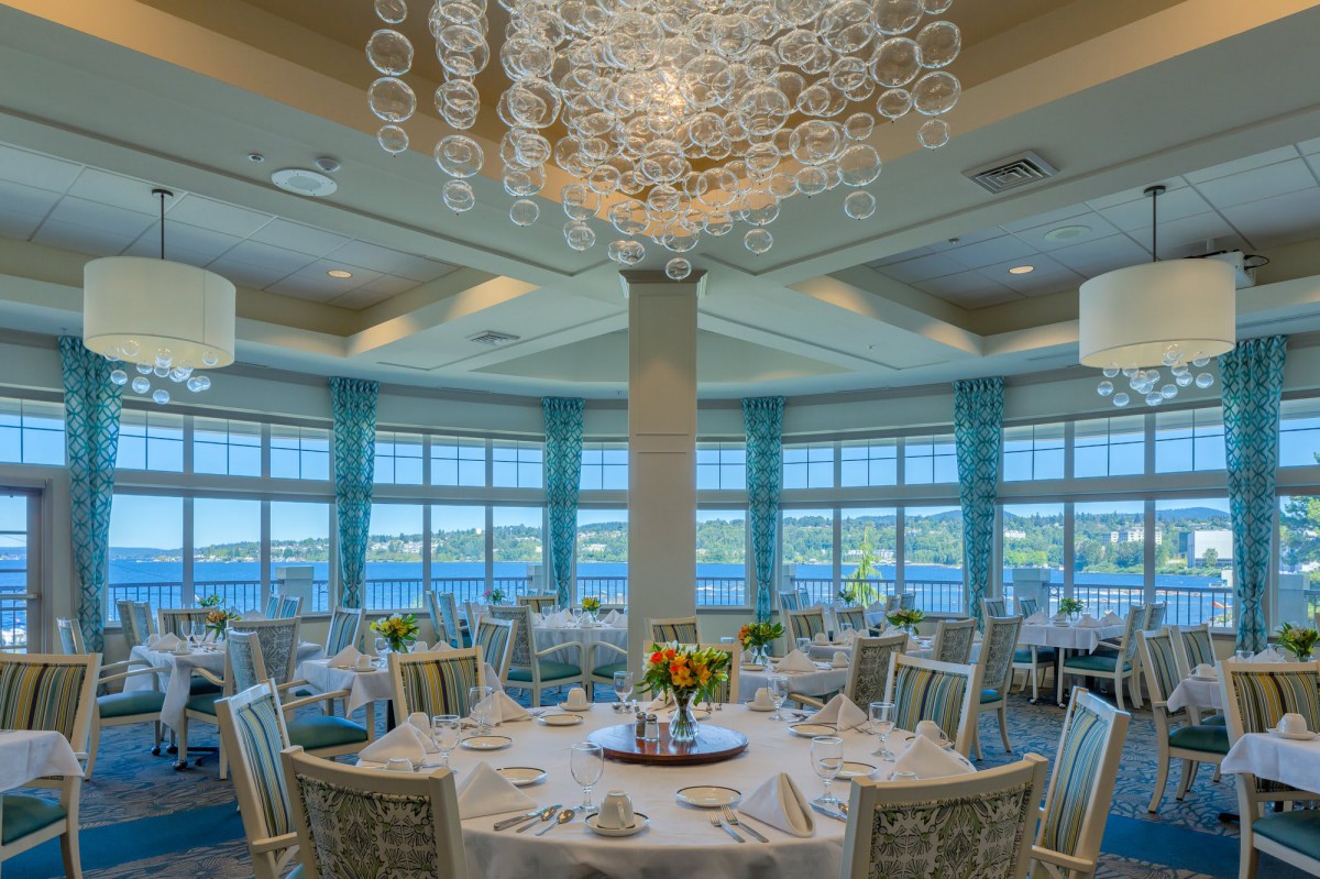 Elegant dining room with beautifully set round tables and a stunning view of the water.