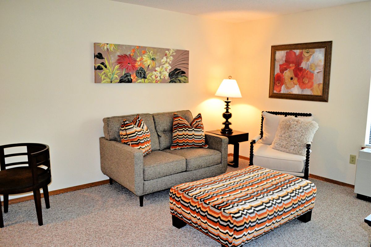 A cozy living room with a sofa, colorful ottoman, and wall art.