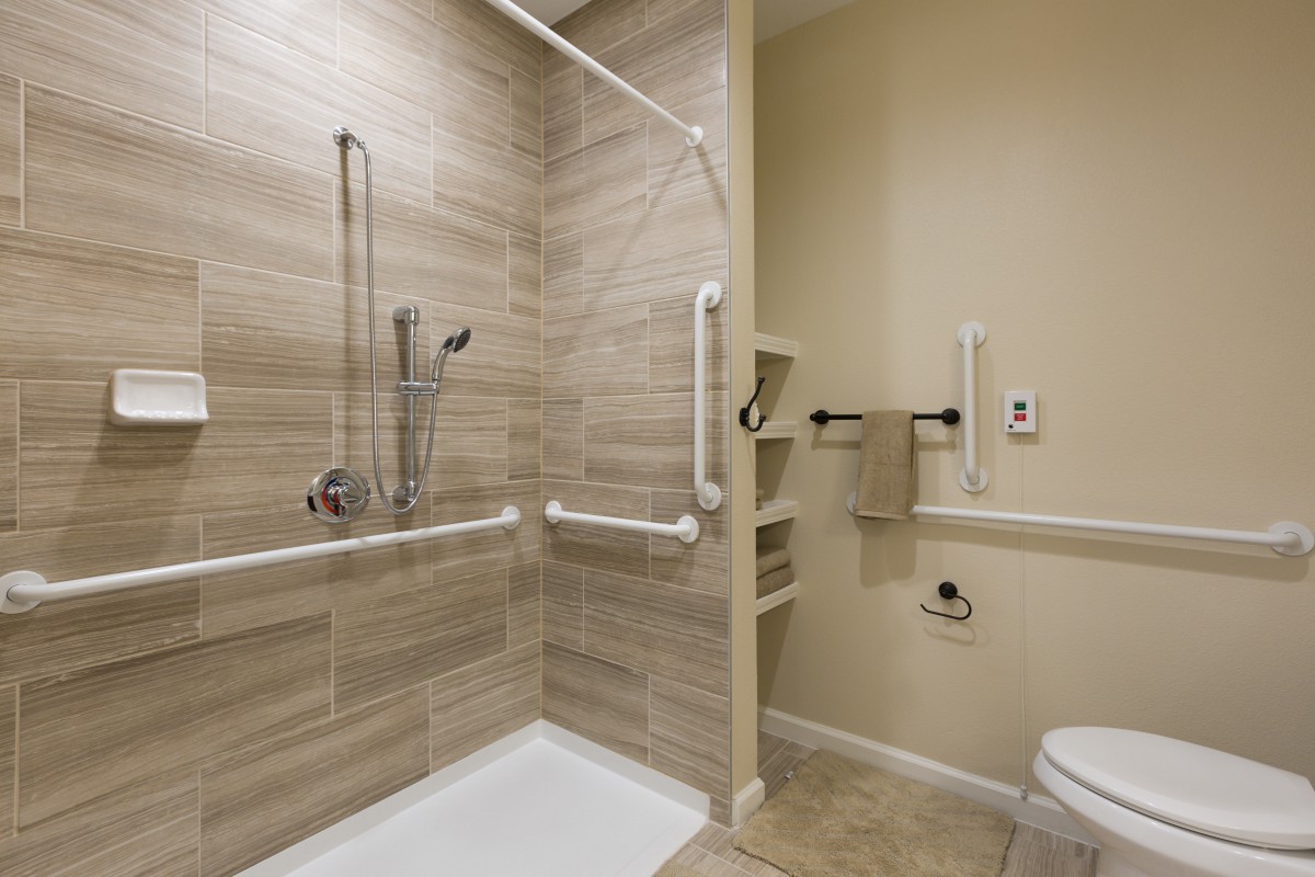 An accessible bathroom featuring a shower with grab bars and a tiled wall.