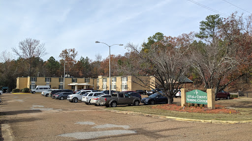 A view of an apartment complex with a parking lot filled with various vehicles and trees in the background.