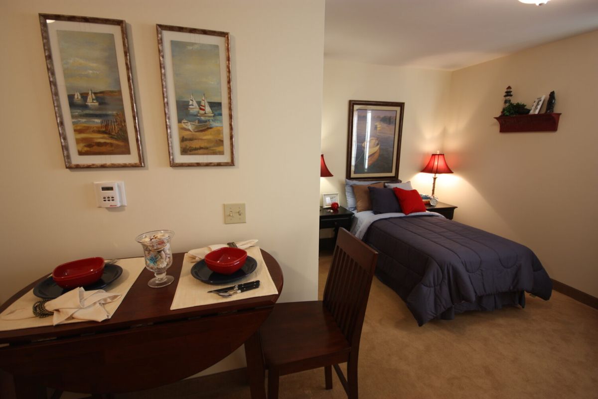 A cozy bedroom with an adjacent dining area, featuring a neatly set table and warm lighting.