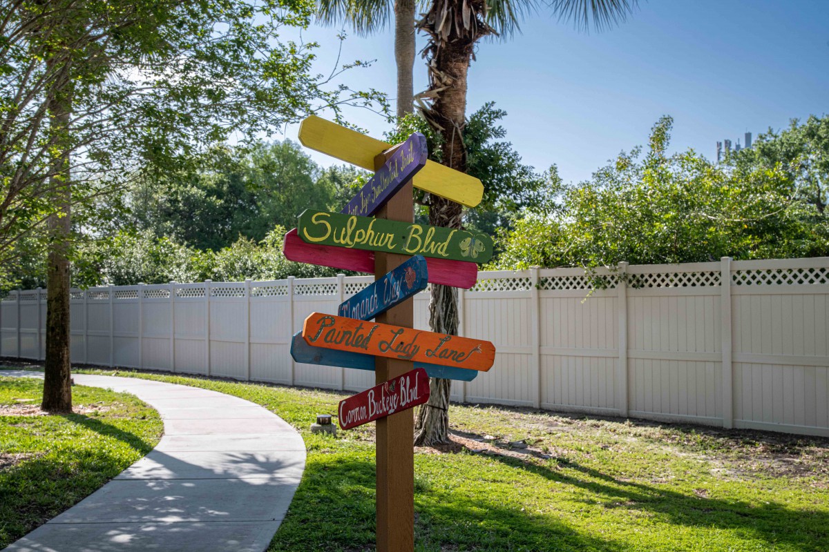 A colorful signpost with multiple directional arrows stands by a pathway in a garden setting.