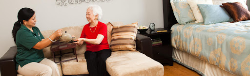 An elderly woman sitting on a sofa, smiling in a cozy living room setting.