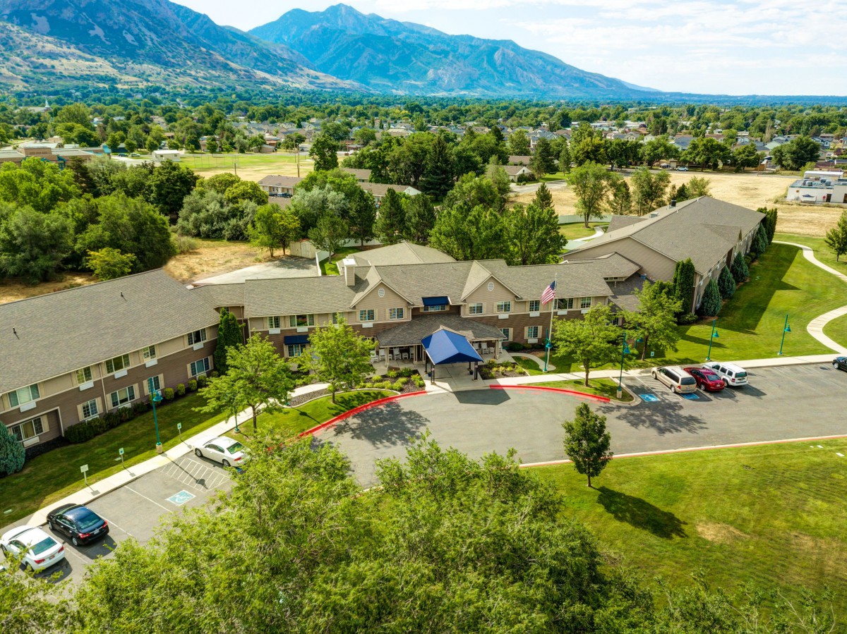 Aerial view of a large building surrounded by trees and mountains, with a parking area in the foreground.
