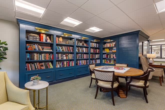 A cozy reading room with blue bookshelves filled with books and a round table surrounded by chairs.