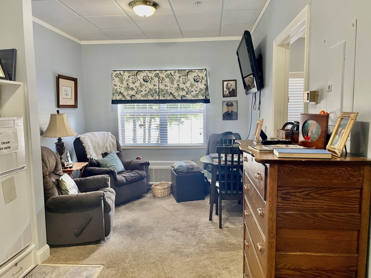 A cozy living room with comfortable seating, a wall-mounted television, and a window adorned with floral curtains.