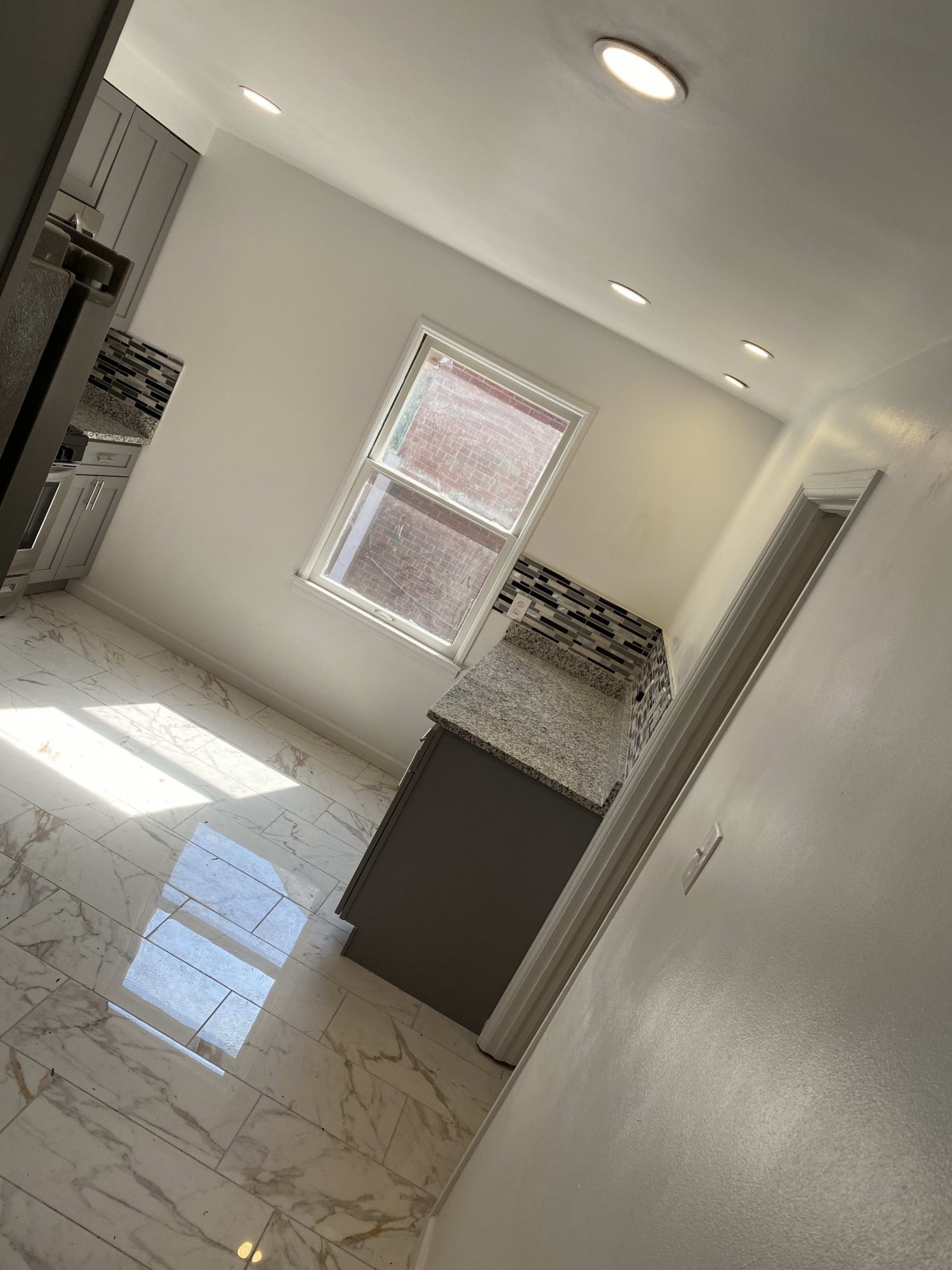 A modern, minimalist kitchen with a marble floor and ample natural sunlight.