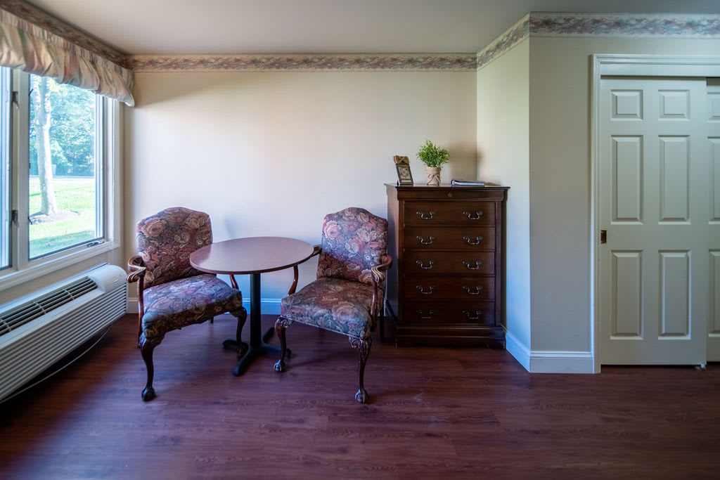 A cozy corner featuring a round table, two upholstered chairs, and a wooden cabinet with a small plant on top.