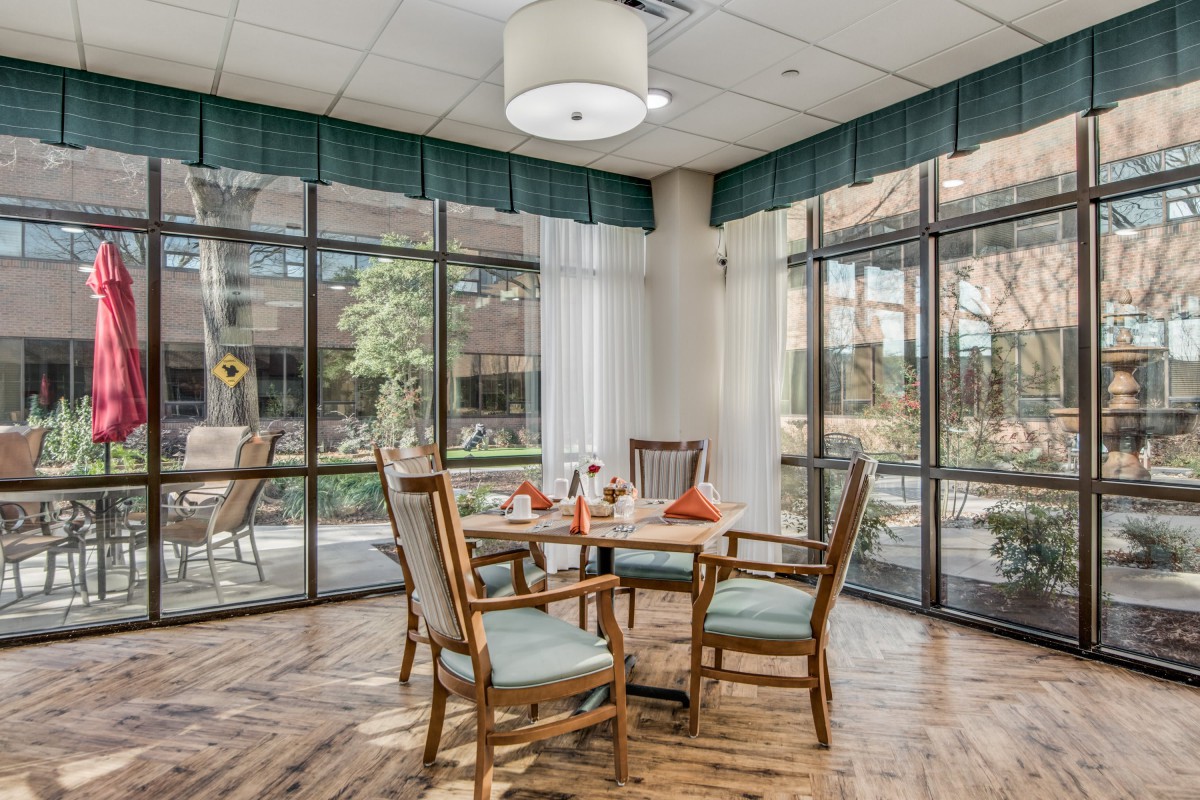 A cozy dining area with a table and four wooden chairs, surrounded by large windows letting in natural light.