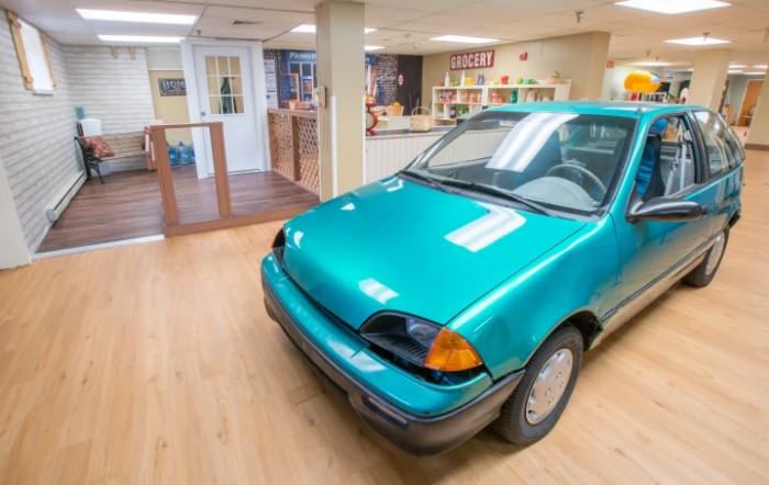 A teal car displayed indoors on a wooden floor.