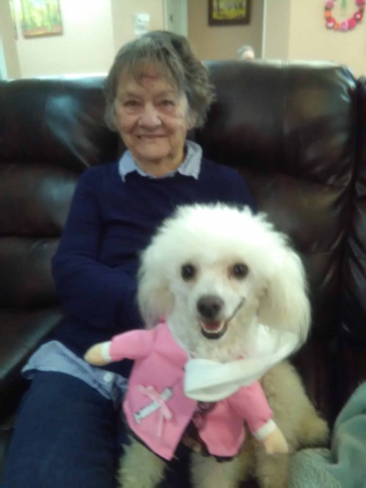 A smiling woman sits on a sofa holding a happy poodle.